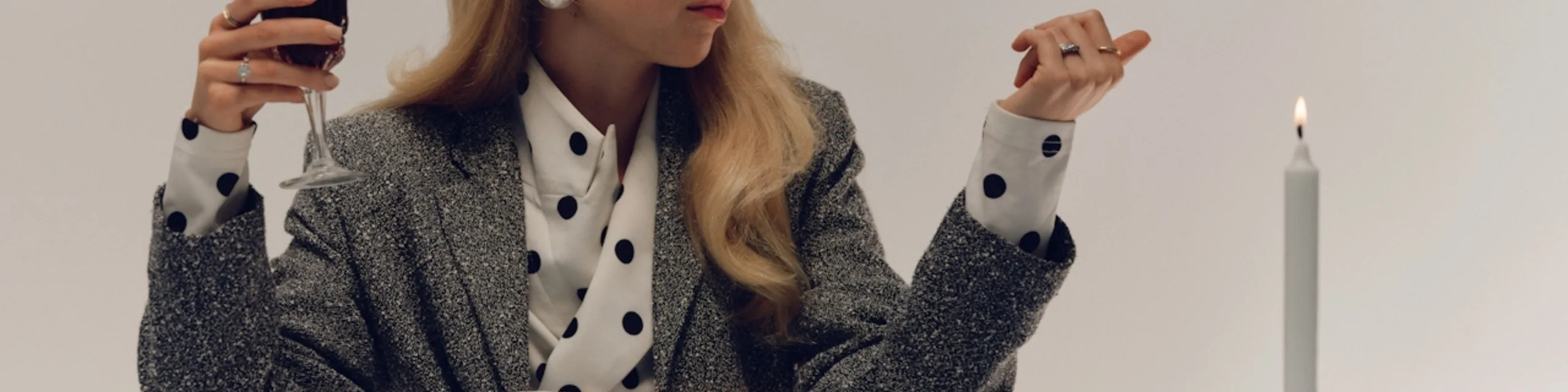 Woman in a polka-dot blouse holding a wine glass beside a lit candle