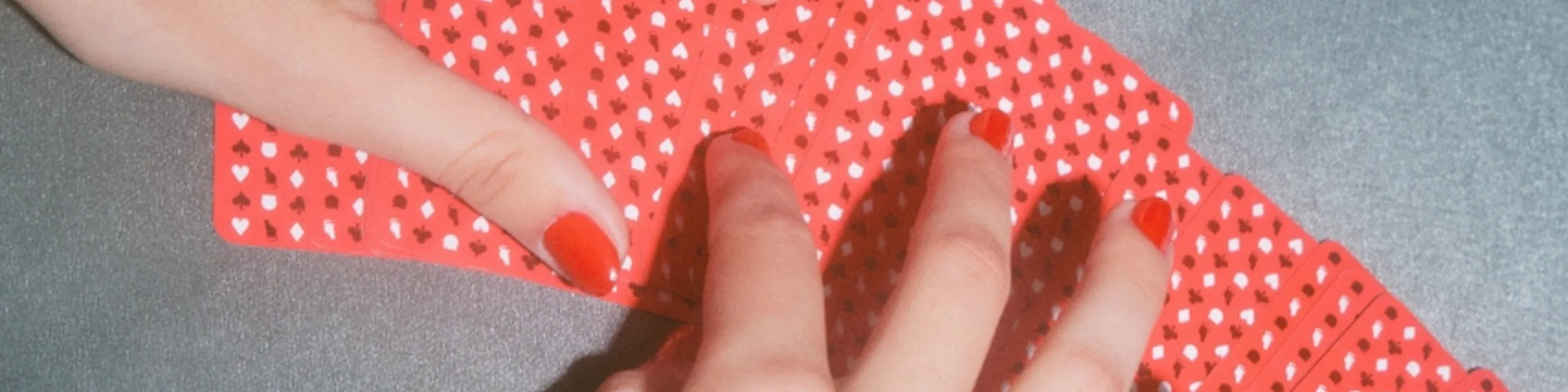Hands fanning a deck of red playing cards across a table